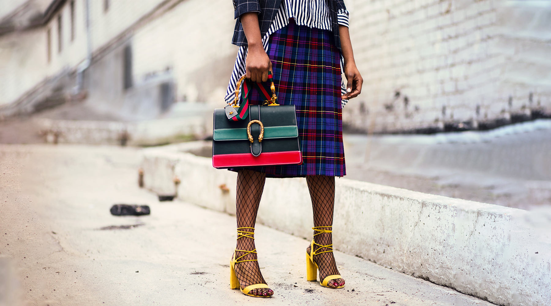 woman in colorful plaid skirt with bright yellow platform sandals and loudly striped purse