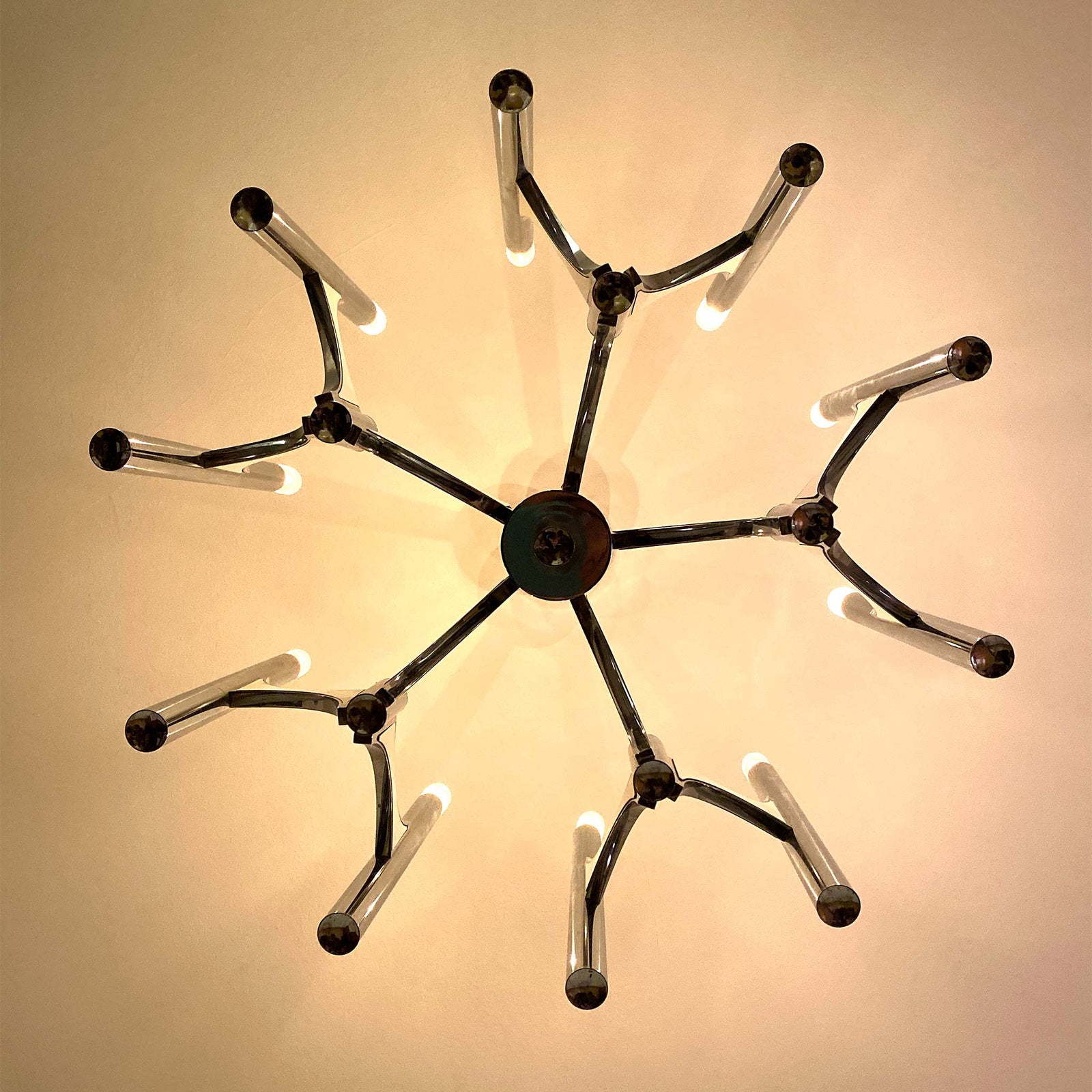 photo of 10-lamp chrome chandelier viewed from below showing five pairs of tube-mounted lamps attached to flying buttress-like arms radiating from central rod from mindscapade